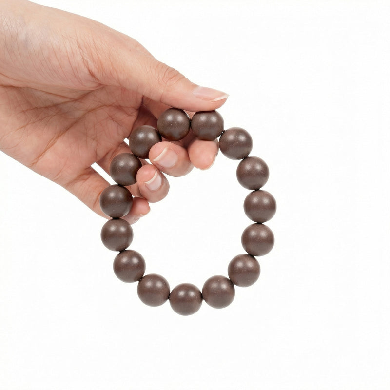 Hand holding a brown beaded bracelet on a white background