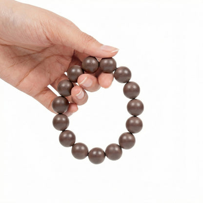 Hand holding a brown beaded bracelet on a white background