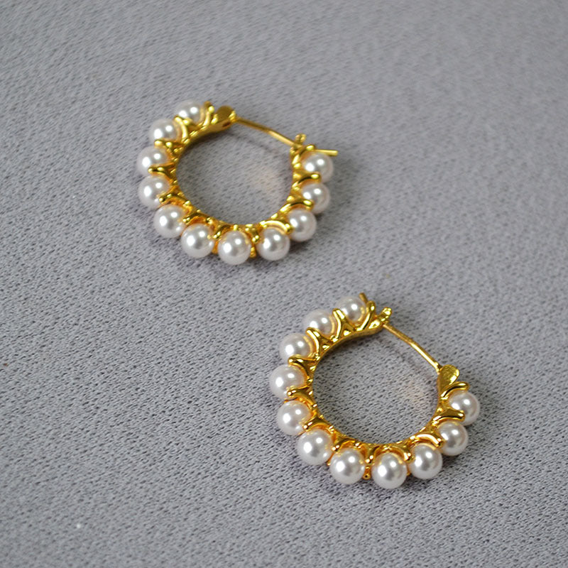 Pair of gold hoop earrings with pearl beads on a gray background
