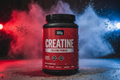 Red creatine powder container with black lid on a colorful background