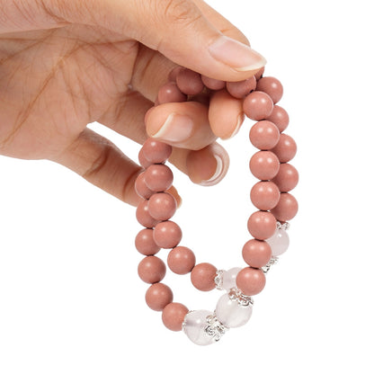 Hand holding a pink beaded bracelet with white beads on a white background