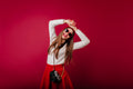 Woman in a white sweater and red skirt posing with a camera against a pink background