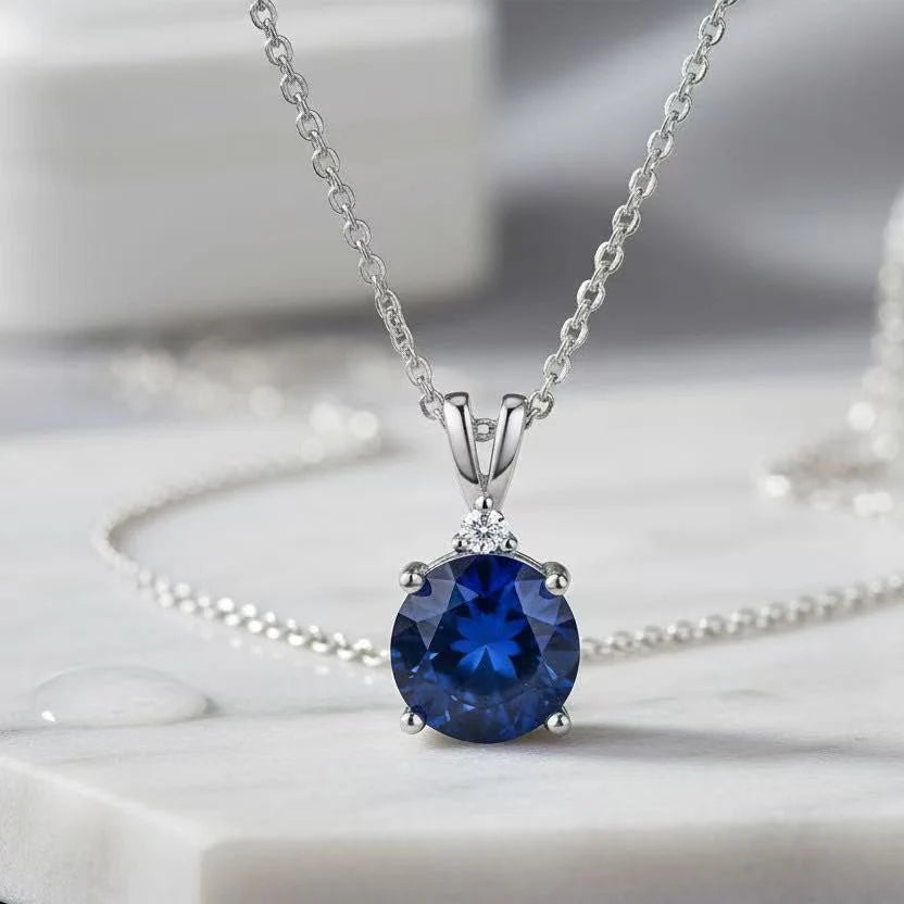 Silver necklace with a blue gemstone pendant on a marble surface